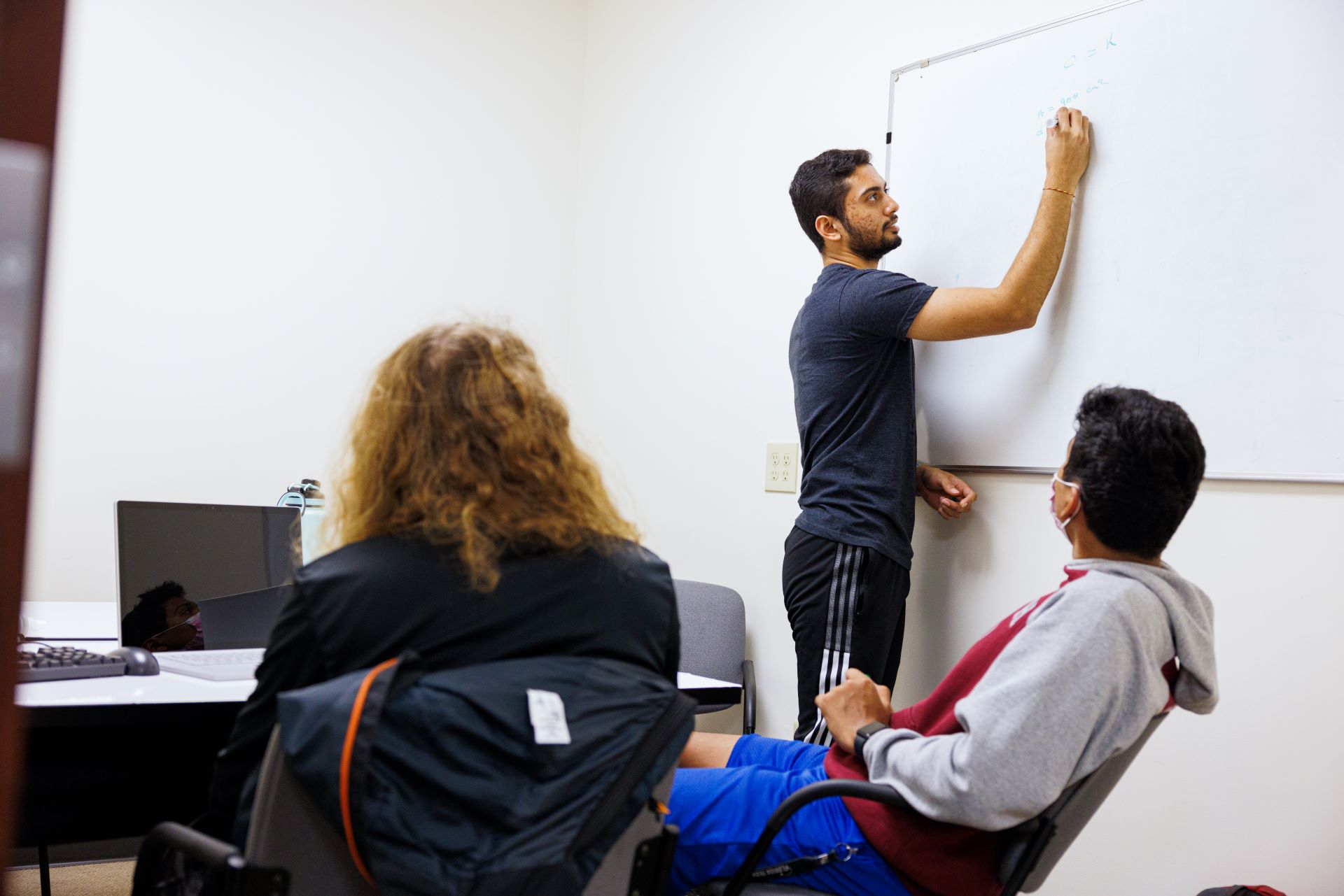 A student writing on a whiteboard while others in the classroom watch